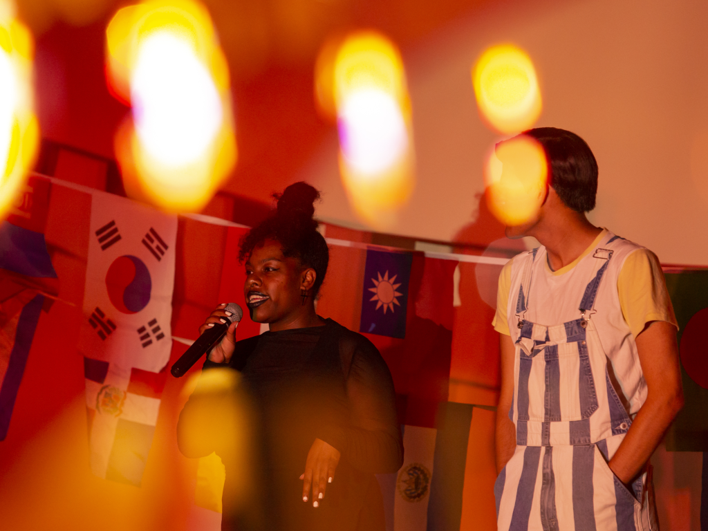 Two students on stage in front of flags from around the world