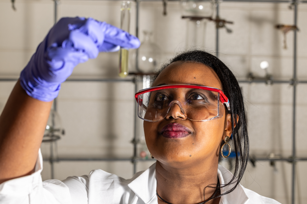 Faith Aynekulu wears protective glasses and gloves to view a chemical in a test tube