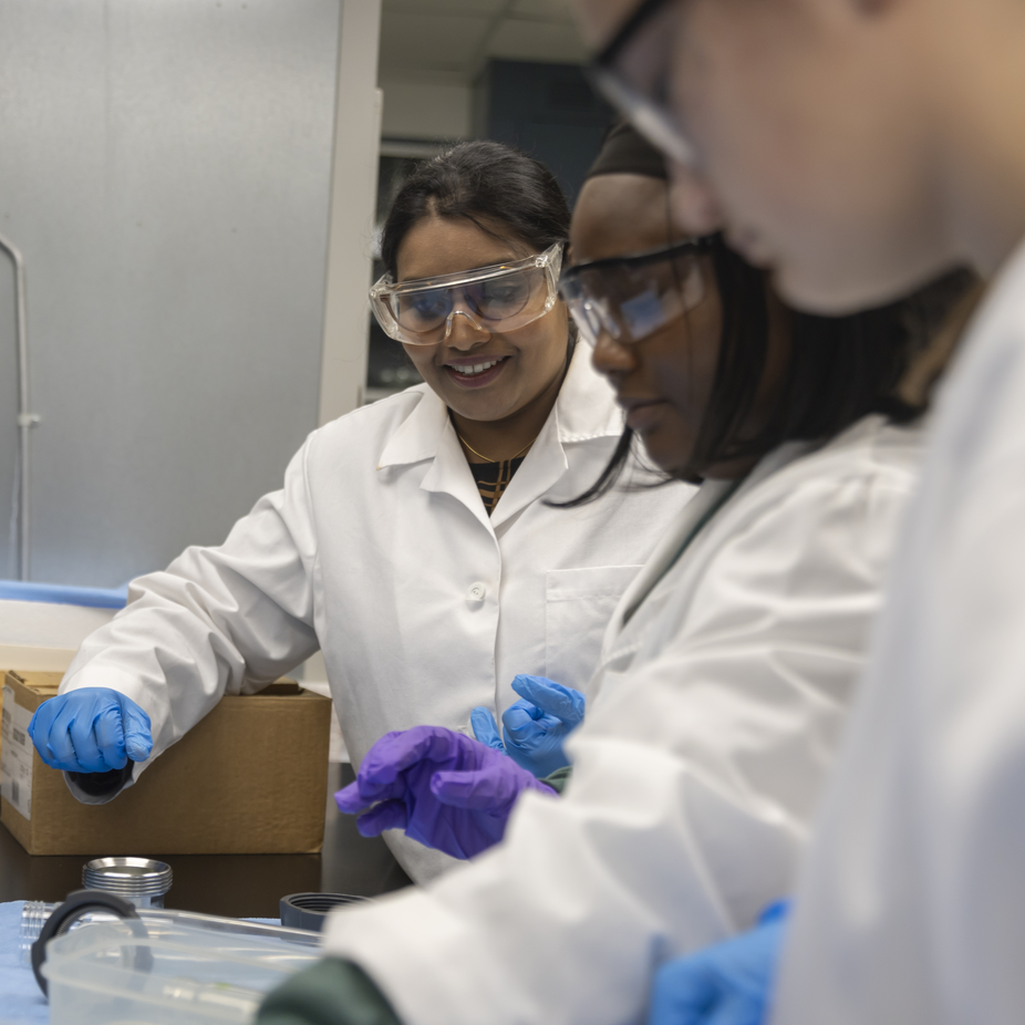 Students wearing lab coats and protective gear work in a lab