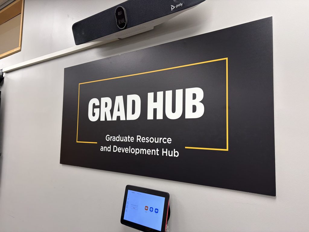A black sign with white text reading Grad Hub: Graduate Resource and Development Hub hanging on a classroom wall